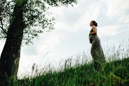 Pregnant woman posing in a green park. young happy pregnant woman relaxing and enjoying life in natureの写真素材