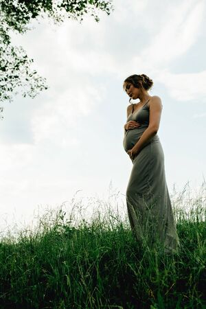 Pregnant woman posing in a green park. young happy pregnant woman relaxing and enjoying life in natureの写真素材