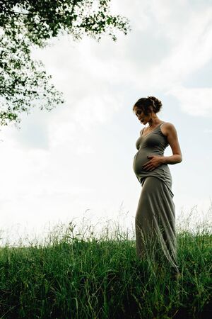 Pregnant woman posing in a green park. young happy pregnant woman relaxing and enjoying life in natureの写真素材