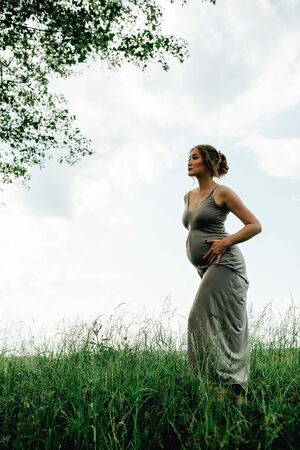 Pregnant woman posing in a green park. young happy pregnant woman relaxing and enjoying life in natureの写真素材