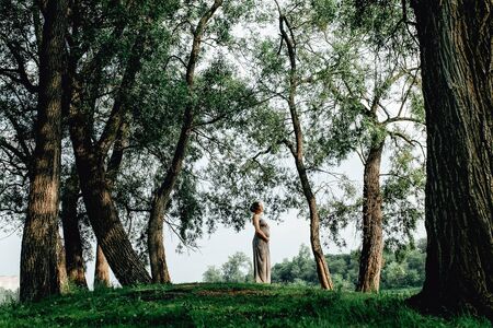 Beautiful pregnant woman walks in the green park along the riverの写真素材