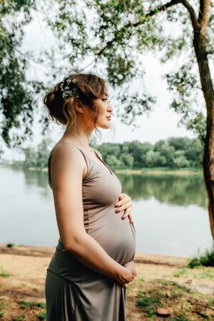 Beautiful pregnant woman walks in the green park along the riverの写真素材