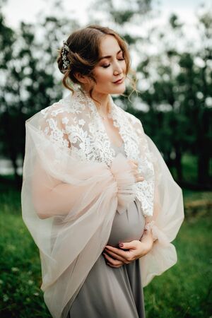 Pregnant woman posing in the park . Portrait of a happy and proud pregnant woman looking at her bellyの写真素材