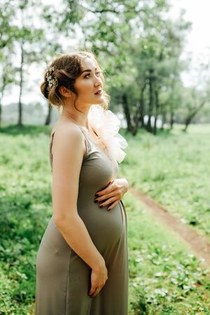 Pregnant woman posing in the park . Portrait of a happy and proud pregnant woman looking at her bellyの写真素材
