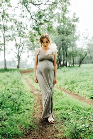 Pregnant woman posing in the park . Portrait of a happy and proud pregnant woman looking at her bellyの写真素材
