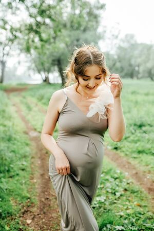 Pregnant woman posing in the park . Portrait of a happy and proud pregnant woman looking at her bellyの写真素材