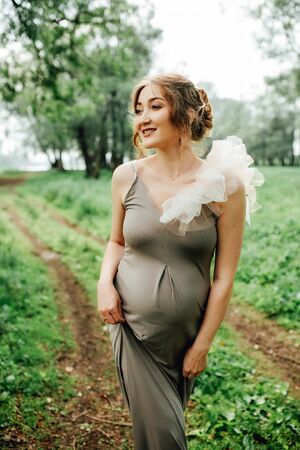 Pregnant woman posing in the park . Portrait of a happy and proud pregnant woman looking at her bellyの写真素材