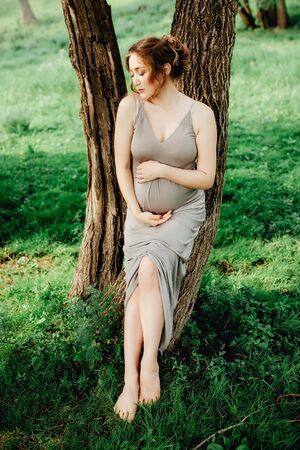 Pregnant woman posing in the park . Portrait of a happy and proud pregnant woman looking at her bellyの写真素材