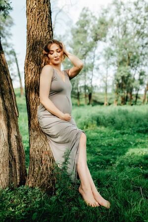 Pregnant woman posing in the park . Portrait of a happy and proud pregnant woman looking at her bellyの写真素材