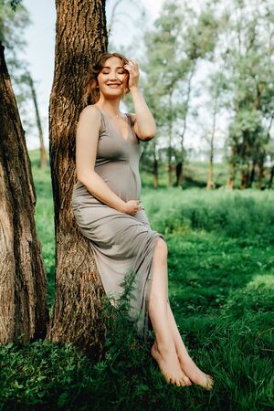 Pregnant woman posing in the park . Portrait of a happy and proud pregnant woman looking at her bellyの写真素材