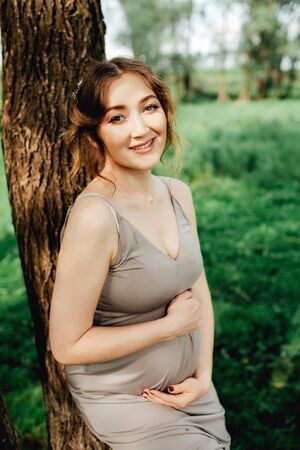 Pregnant woman posing in the park . Portrait of a happy and proud pregnant woman looking at her bellyの写真素材