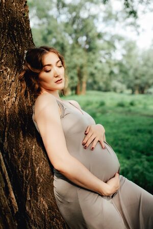 Pregnant woman posing in the park . Portrait of a happy and proud pregnant woman looking at her bellyの写真素材