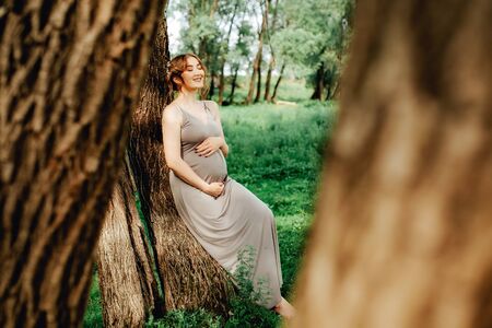 Pregnant woman posing in the park . Portrait of a happy and proud pregnant woman looking at her bellyの写真素材