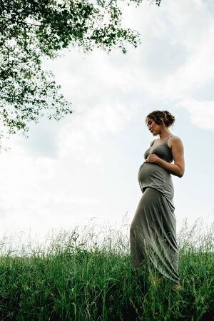 Pregnant woman posing in a green park. young happy pregnant woman relaxing and enjoying life in natureの写真素材