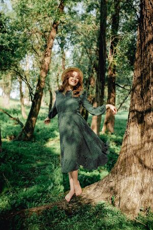 Smiling pretty pregnant woman touching around the abdomen against greenery background. Wearing green dress and summer hatの写真素材