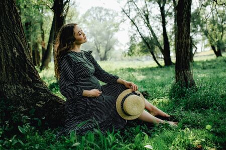 Pregnant woman posing in a green park. young happy pregnant woman relaxing and enjoying life in natureの写真素材