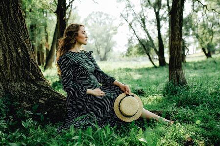 Pregnant woman posing in a green park. young happy pregnant woman relaxing and enjoying life in natureの写真素材
