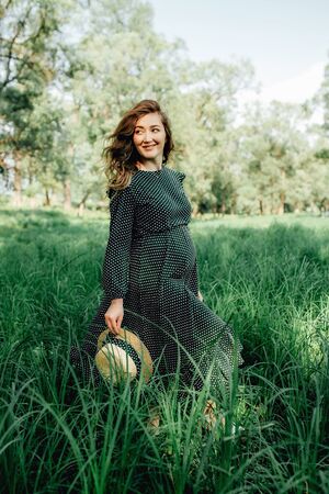Pregnant woman posing in a green park. young happy pregnant woman relaxing and enjoying life in natureの写真素材