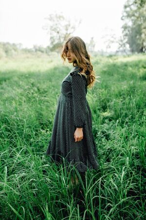 Smiling pretty pregnant woman touching around the abdomen against greenery background. Wearing green dress and summer hatの写真素材