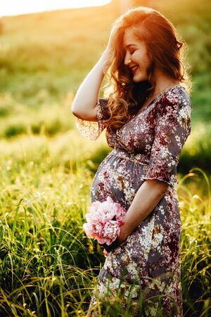 Pregnant woman feeling happy with new life at summer field while take care of her child. The young expecting mother holding baby in pregnant belly. Maternity prenatal care and woman pregnancy concept.の写真素材