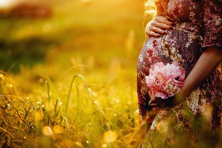 Close up of pregnant woman are relaxing in the garden at sunset. pregnant woman holding her belly and flower in the garden.の写真素材