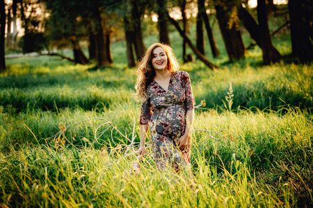 Pregnant woman feeling happy with new life at summer field while take care of her child. The young expecting mother holding baby in pregnant belly. Maternity prenatal care and woman pregnancy concept.の写真素材