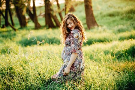 Pregnant woman feeling happy with new life at summer field while take care of her child. The young expecting mother holding baby in pregnant belly. Maternity prenatal care and woman pregnancy concept.の写真素材