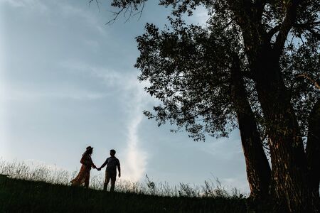 Stylish pregnant couple silhouettes in sunny light in park among grass. Happy young parents, mom and dad, enjoying beautiful moment at sunset. Parenthood conceptの写真素材