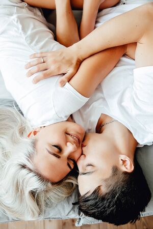 young lovely couple lying in a bed, happy smile looking to each other, top view.の写真素材
