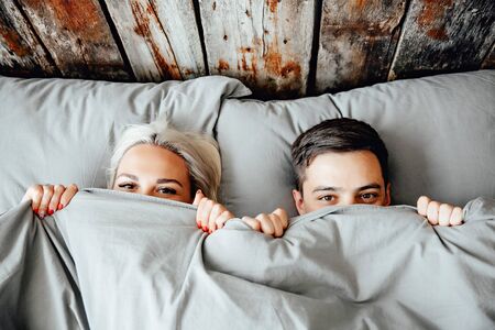 young lovely couple lying in a bed, happy smile looking at camera, cover under blanket top angle view up aboveの写真素材
