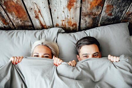 young lovely couple lying in a bed, happy smile looking at camera, cover under blanket top angle view up aboveの写真素材