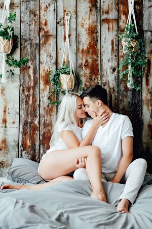 Portrait of romantic couple sitting on bed in bedroomの写真素材