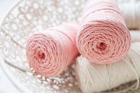 Handmade macrame braiding and cotton threads in white basket. Cotton macrame cords and ropes against wire basket. Good image for macrame and handicrafts banners and advertisement. Close upの写真素材