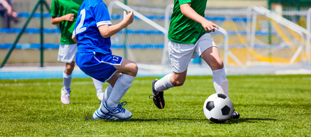 Children Soccer Players Running with the Ball. Kids in Blue and Green Soccer Jerseys Playing Football on the Pitch. Sports Stadium in the Backgroundの写真素材