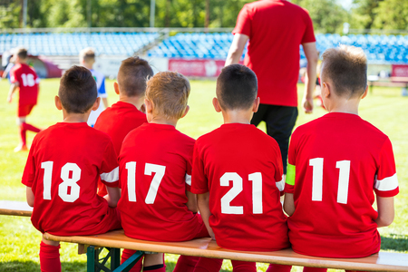 Kids Soccer Team. Youth Football Players with Soccer Coach. Young Substitute Player Sitting on Wooden Bench.の写真素材