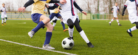 Two youth footballers running the ball. Junior football match. Boys Boys playing soccer match on professional football pitch. Football Stadium in the Backgroundの写真素材