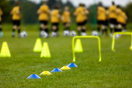 Football Training Session. Soccer Balls, Pylons, Cones, Marks and Training Hurdles on Grass Pitch. Youth Soccer Player Training. Young Footballer with Ball Training on a Green Sports Fieldの写真素材