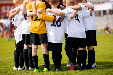 Kids sports team with coach. Team sports for children. Young boys standing together as a teammates having team briefing huddle with coach. Youth coach motivating team members before the matchの写真素材