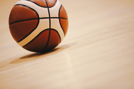 Basketball on Wooden Court Floor Close Up with Blurred Arena in Background. Orange Ball on a Hardwood Basketball Courtの写真素材