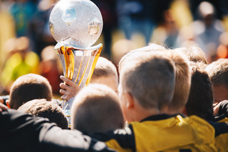Kids Sport Team with Trophy. Kids Celebrating Football Championship. Happy Young Soccer Players Holding Golden Cup. Football Team Winning Youth Soccer Tournamentの写真素材