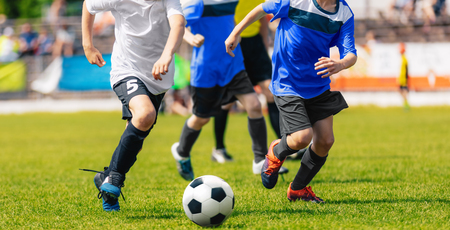 Boys running and kicking soccer ball. Close up action of boys soccer teams, aged 8-10, playing a football match on the stadiumの写真素材