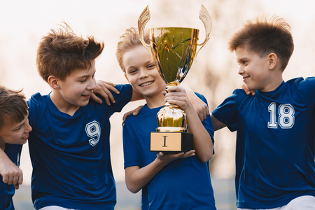 Boys sports team celebrating victory. Happy children holding golden trophy. Kids football team raising winners' cup.  Youth sports successの写真素材
