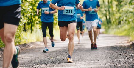 Group of runners running fast through the forest on trail marathon run