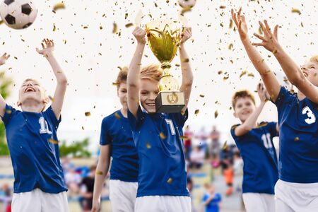 Champion youth soccer team with winning trophy. Boys football team celebrating victory in school competition by rising up golden cup. Happy kids as soccer tournament winnersの写真素材