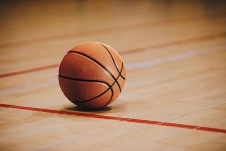 Classic Basketball on Wooden Court Floor Close Up with Blurred Arena in Background. Orange Ball on a Hardwood Basketball Courtの写真素材