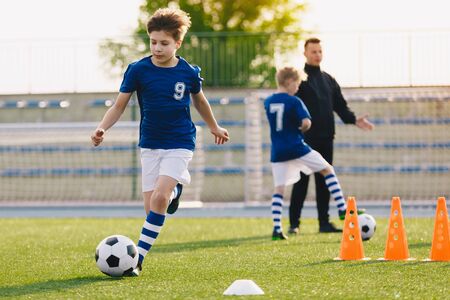 10 year old boy running soccer ball. Elementary age school kids on football training with young coach. Children sports team improving dribbling speed and agility skills on session with training conesの写真素材