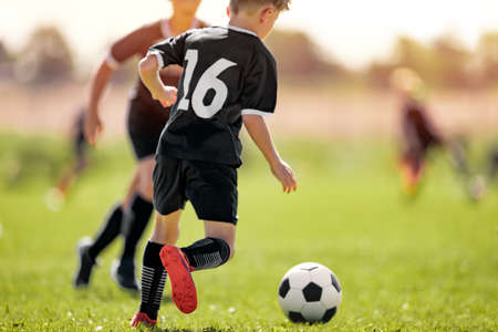 Kids in Soccer Club. Sports Summer Training Camp for School Children. Sports Summer Activity for Junior Level Athletes. Boy Running After Ball on Grassの写真素材