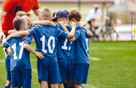 Kids in elementary school sports team with coach. Boys in blue soccer uniforms with white numbers on...