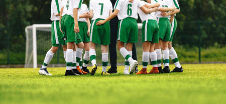 Teenagers in sports team with coach. Soccer briefing with trainer. Boys in uniforms with numbers on back. Coach motivate junior football players before the game. School sports tournament for youthの写真素材