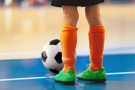 Futsal training for youth team. Young boy with soccer ball standing on white line. Indoor football soccer school practice. Kid in sportswear, black shorts, soccer cleats and orange socksの写真素材